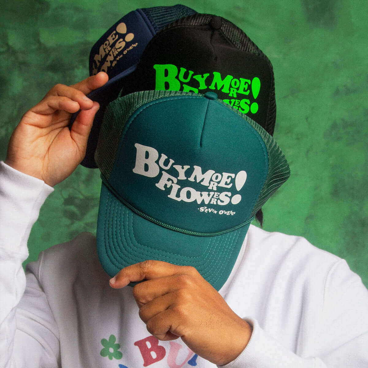 Two Buy More Flowers trucker hats in different colors, showcasing the bold message and unique style.