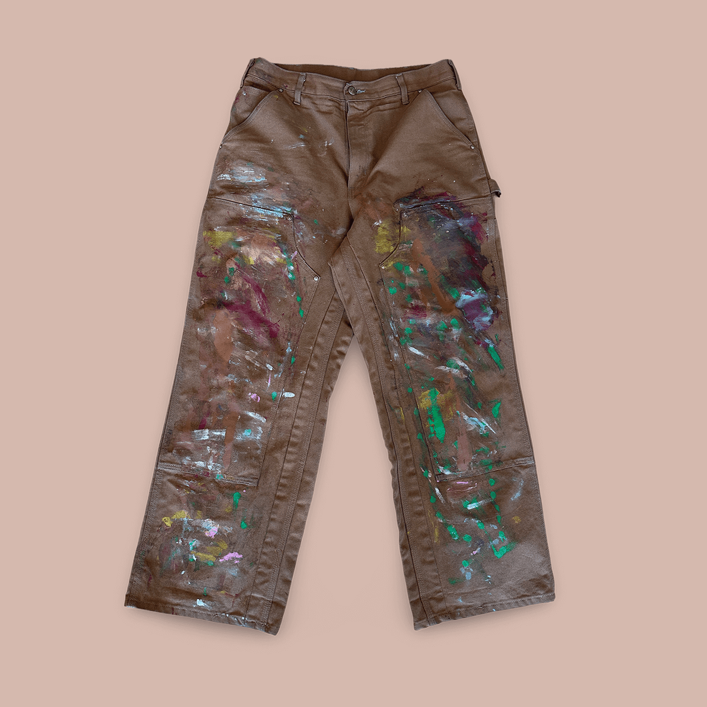 Hand painted work pants with colorful splashes on a brown fabric background, showcasing unique artistic design.